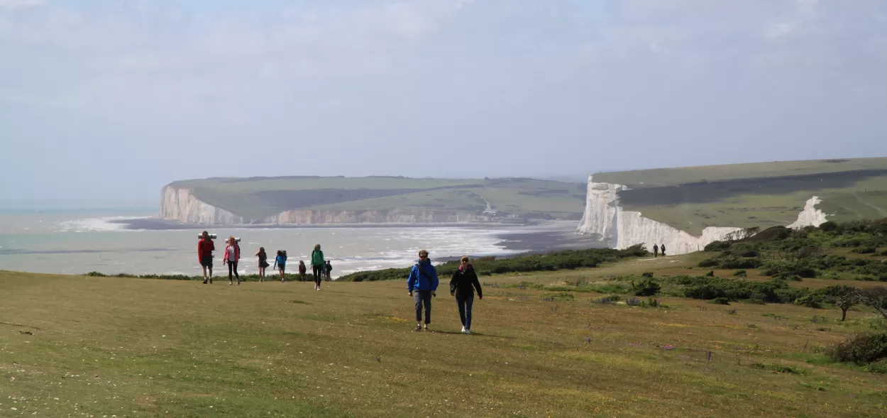 Students walking across the grass with the Seven Sisters chalk cliffs in the background.