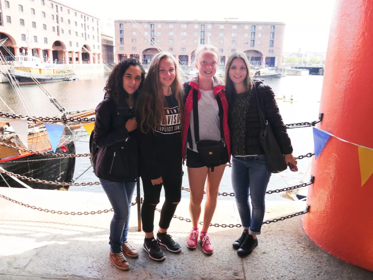 ELC English students on a summer excursion to Liverpool. Here we see four students standing by the edge of the Albert Dock with the water behind them. In the background are buildings which were once the warehouses where goods were stored to be sent overseas or having been imported into England.