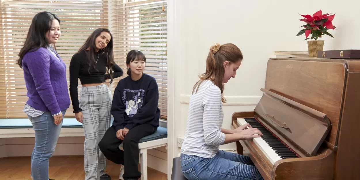 Three English students look on whilst a fourth plays piano during a break in English lessons at ELC English Language School. The piano is always there and available in the student lounge, though maybe not if all you know is "Chopsticks".