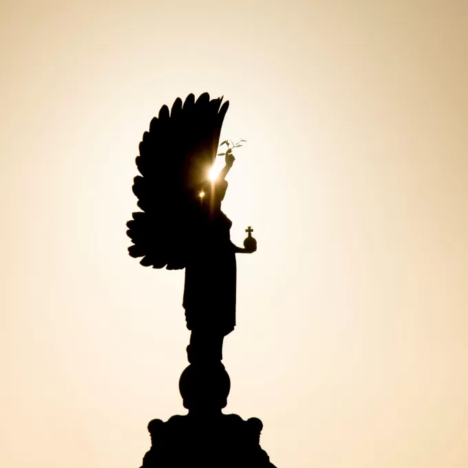 A photo of the peace statue in Brighton, not far from ELC English language school. The sun is directly behind the statue, so we see the wings of the angel, which represents the entirety of the statue, in silhouette. The sky behind is beautiful pale yellow colour.