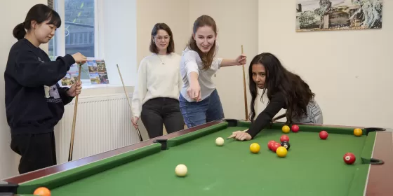 Four students are playing a doubles match of pool on the pool table at ELC Eastbourne. This, along with the tabletennis table is a popular option in the school during breaks between English lessons.