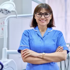 A photo of a medical professional looking at the camera. She's wearing a blue short-sleeved top, she has her arms folded and she's smiling at the person taking the photo.
