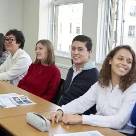 A group of students sit in a row during their English class in Brighton. They looking quite cheerful and it looks like they're about to start a speaking exercise